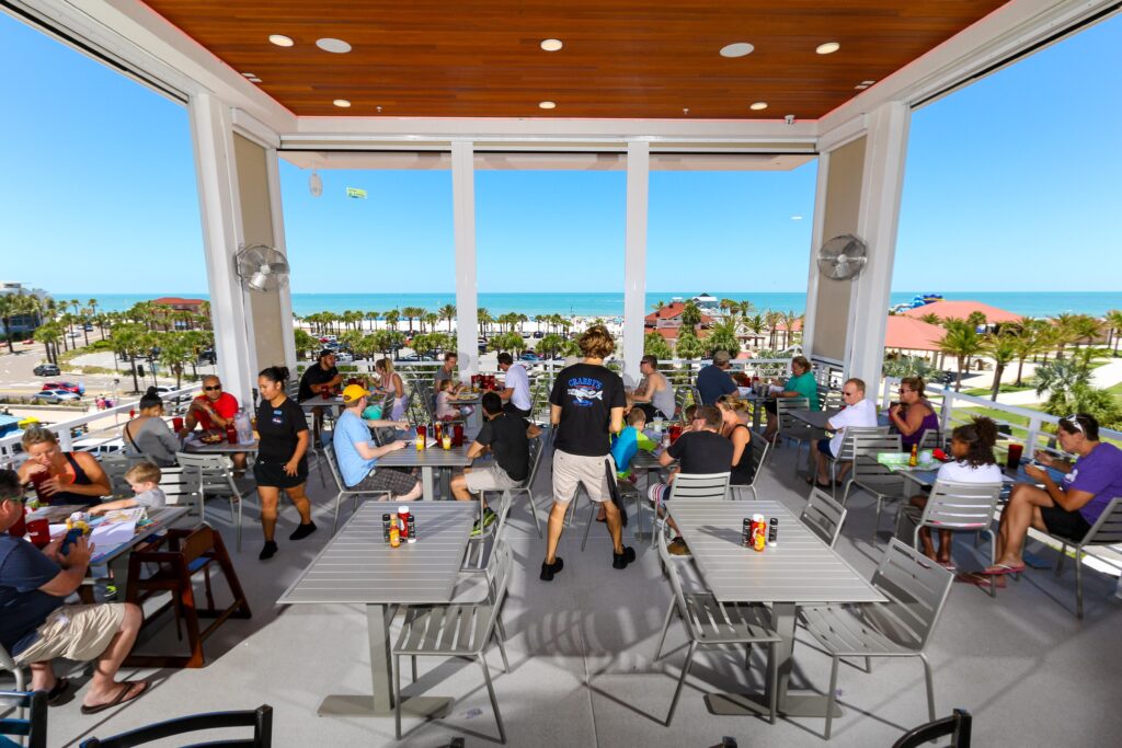 A waiter serving guests in Crabbys Dockside with a view of the Gulf of Mexico behind.